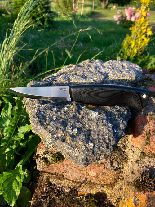 Bushcraft knife with black G10 handle, side view on stone